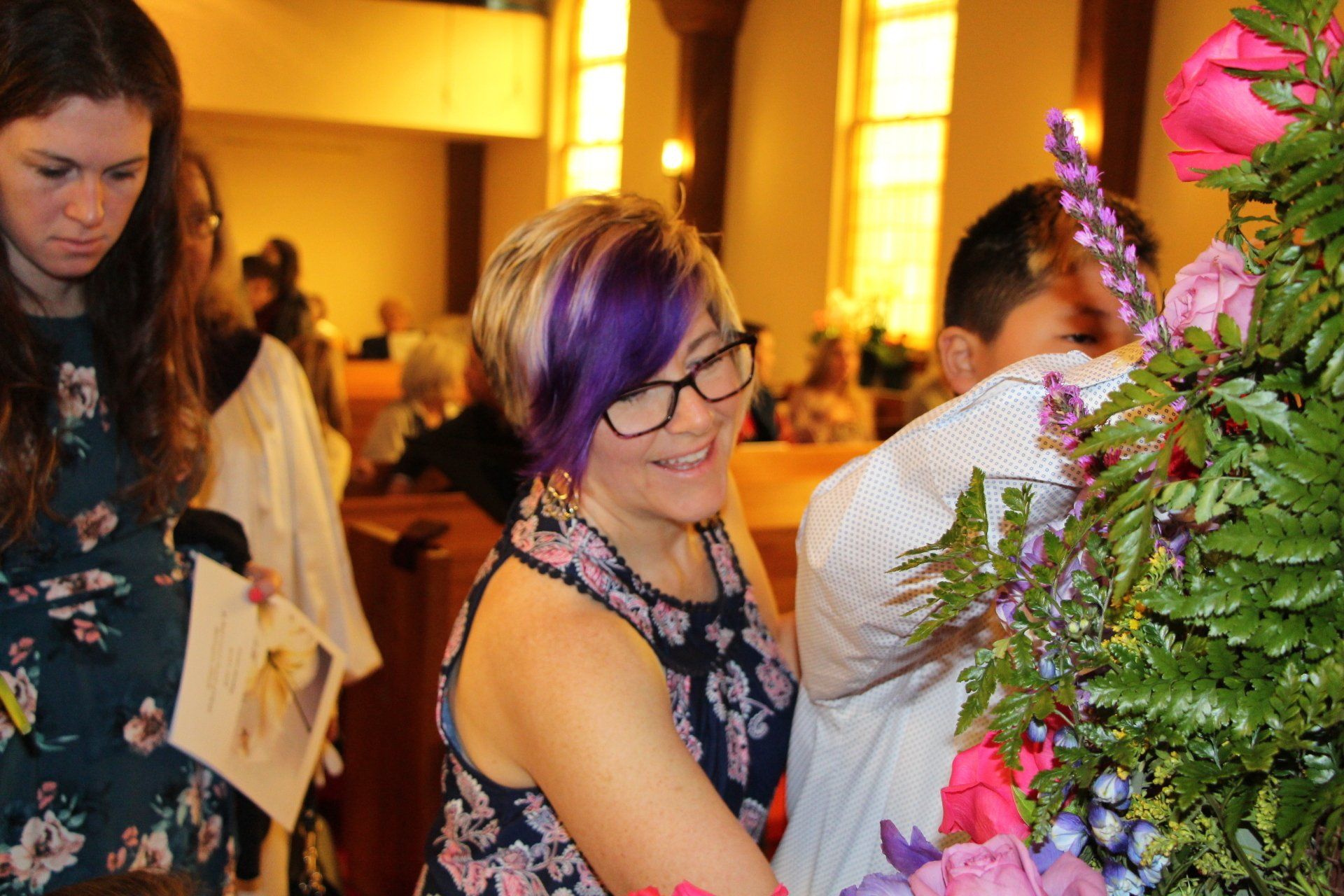 A woman with purple hair is putting flowers on a man 's shirt in a church.