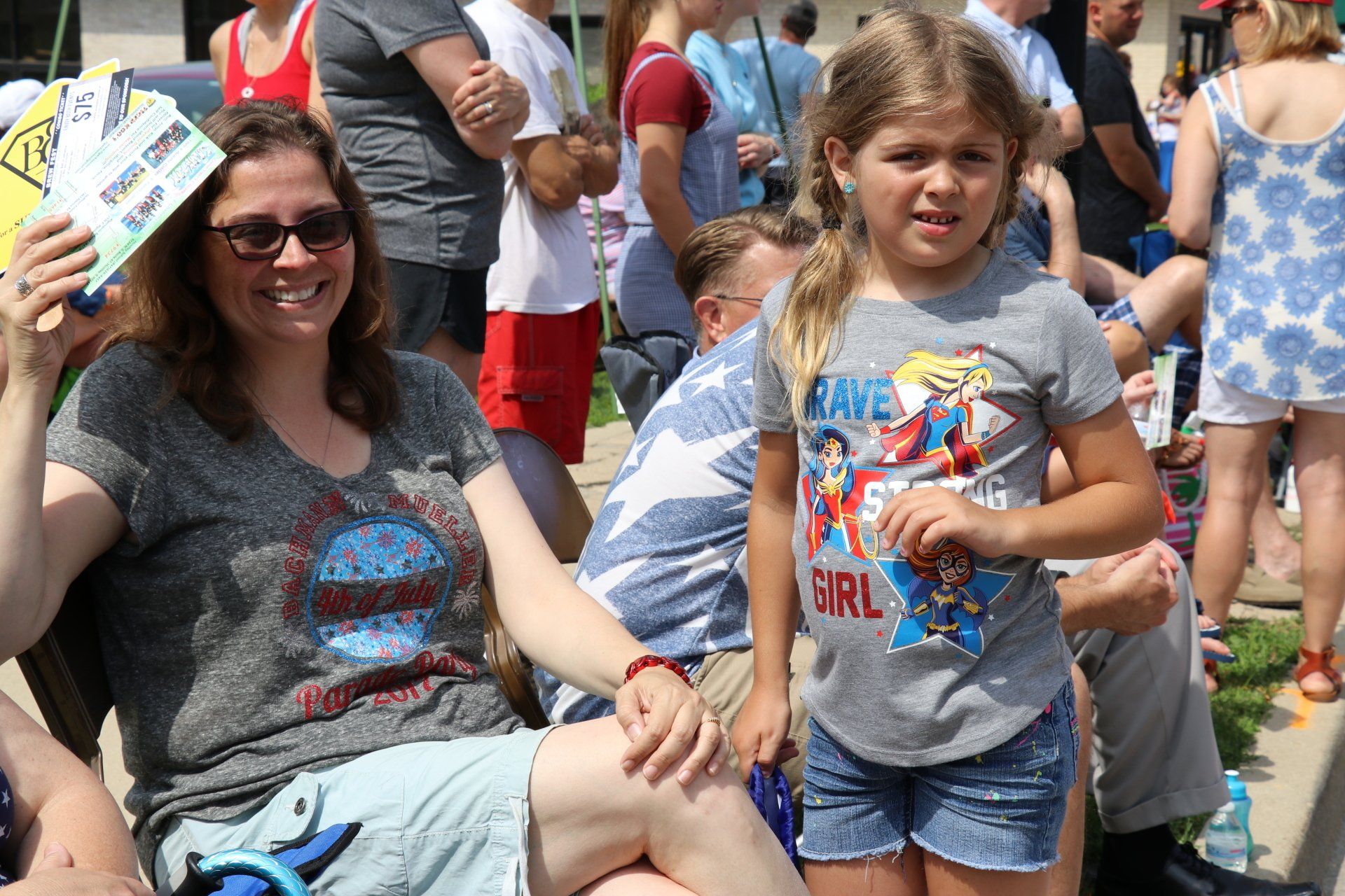 A woman is sitting next to a little girl wearing a superhero shirt.