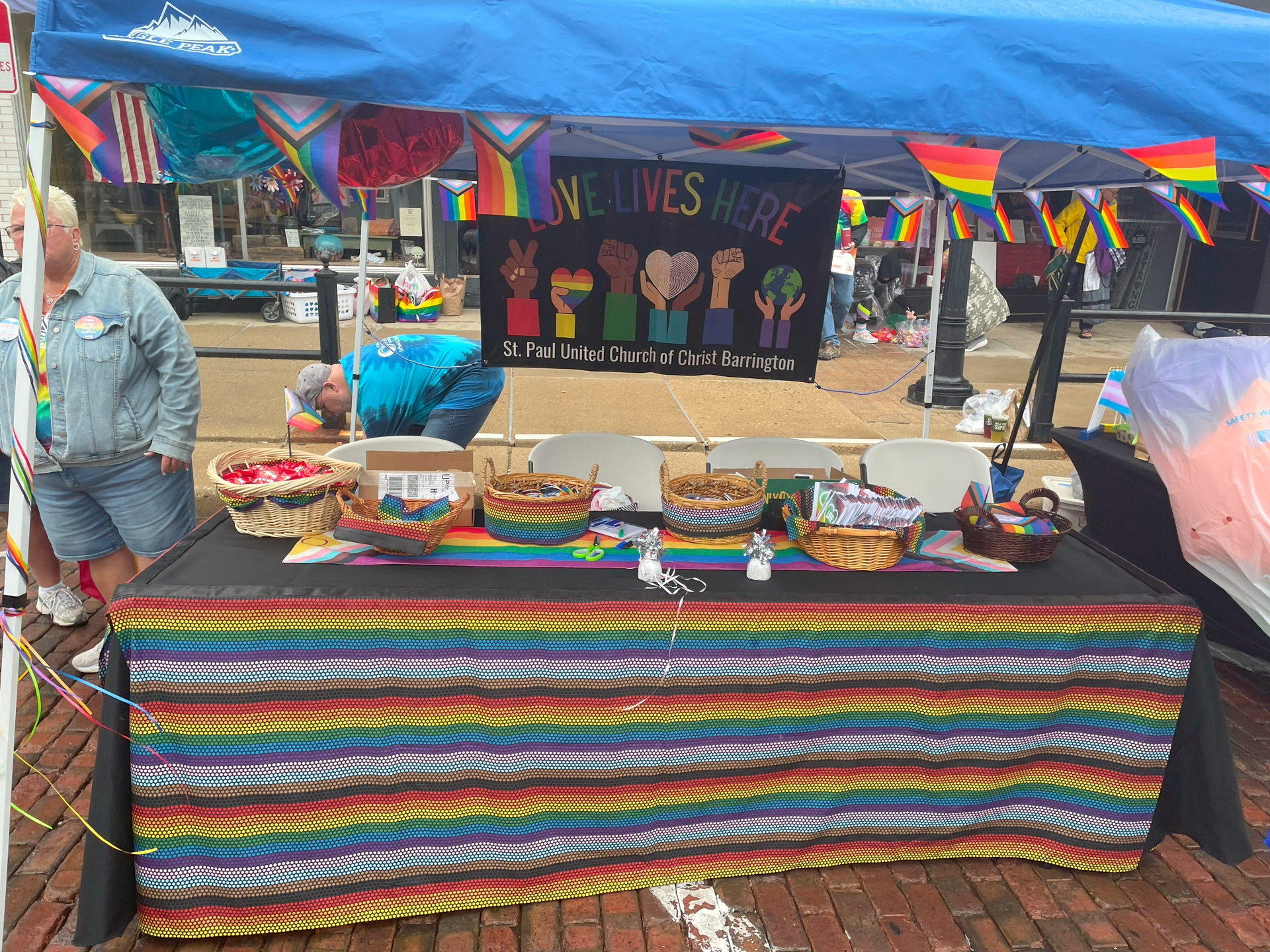 A table with a rainbow tablecloth is under a blue tent.