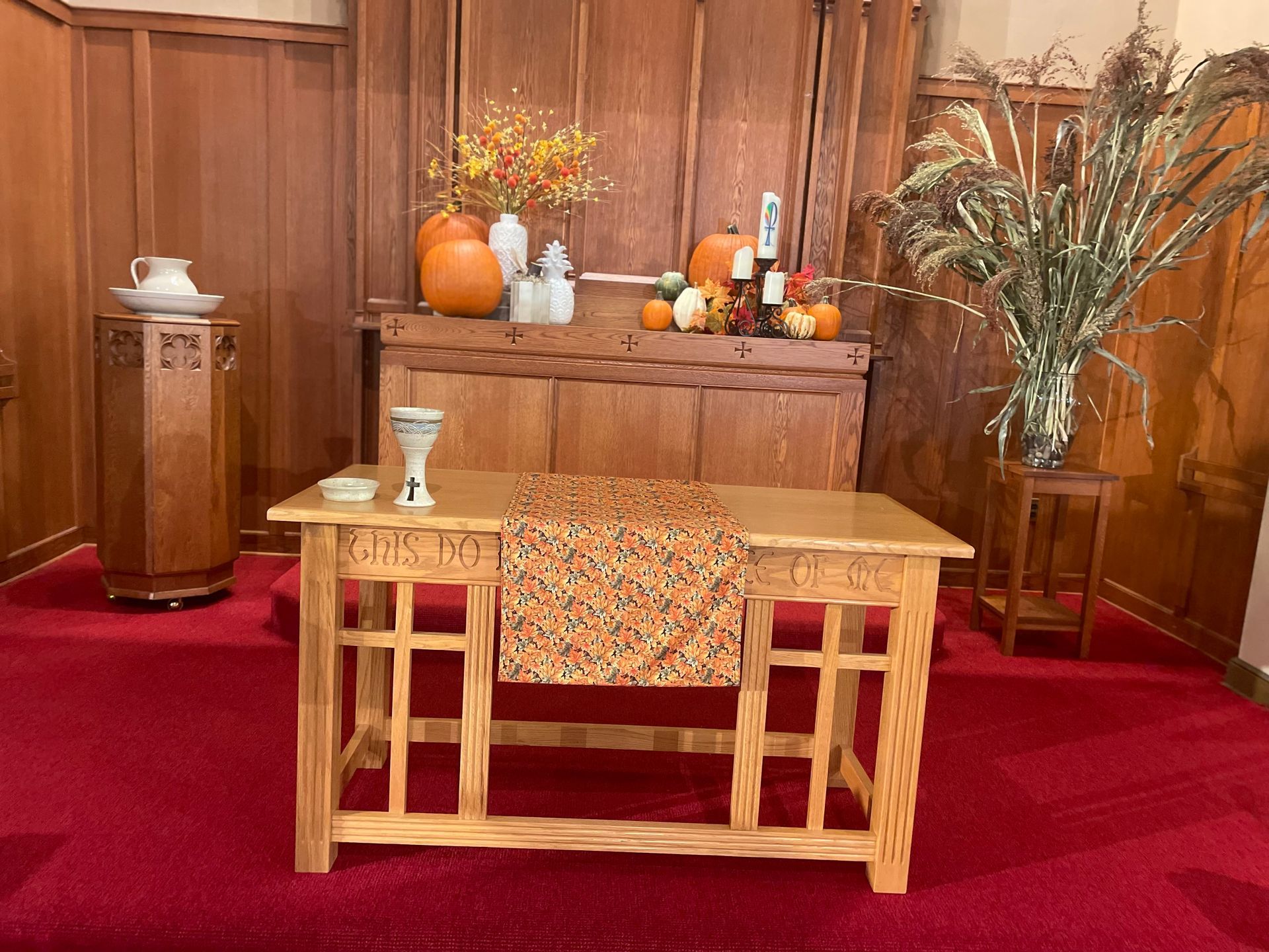 A wooden table with pumpkins and flowers on it in a church.