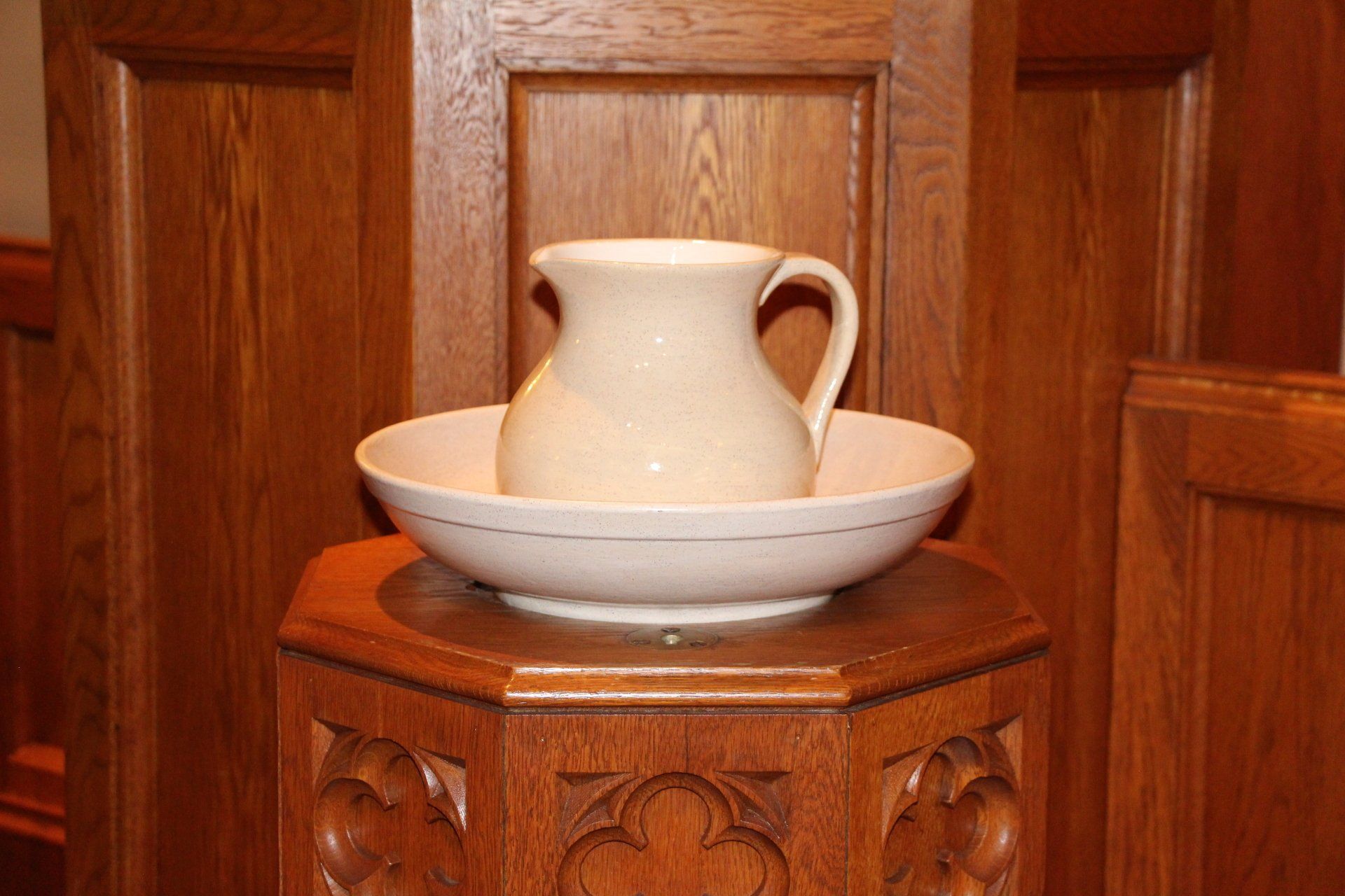 A pitcher and bowl are sitting on a wooden pedestal.