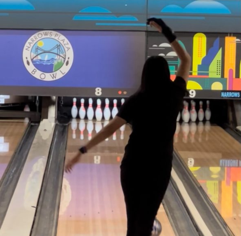 Woman in black outfit bowling at Narrows Plaza Bowl. Her arm is raised after releasing the ball.