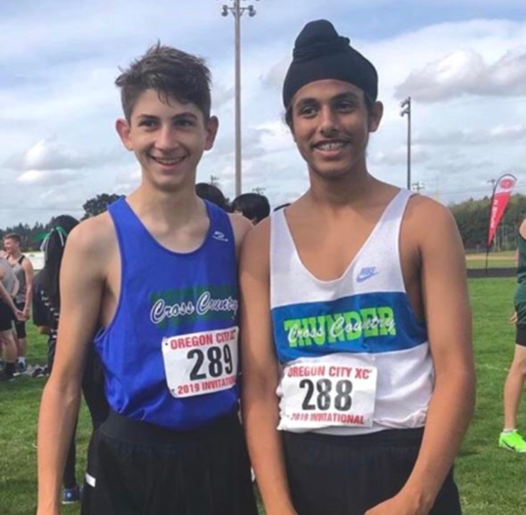 Two young cross-country runners, bib numbers 289 and 288, smiling on a grassy field.