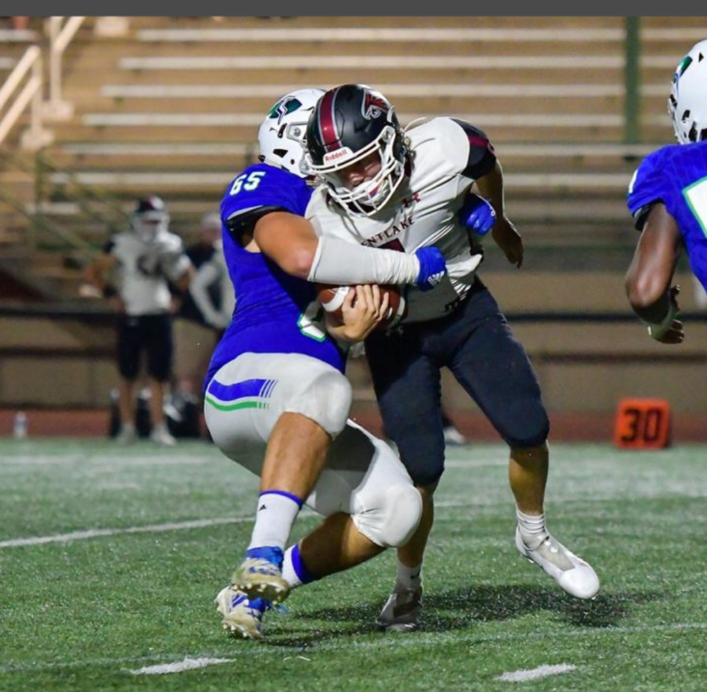 Football player in maroon tackling a player in blue uniform on a green field.