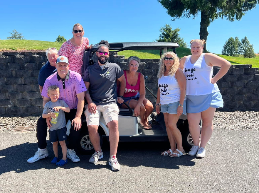Group of people posing by a golf cart on a sunny day; some are smiling.