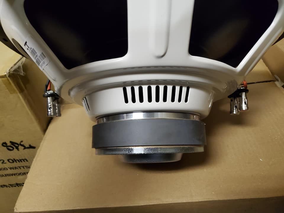 A close-up view of a white subwoofer speaker, showing its vents, gray surround, and mounting brackets.