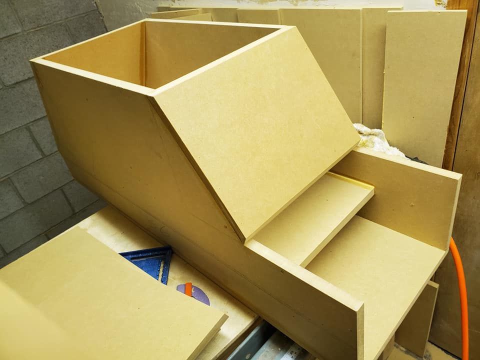 Assembled wooden box structure with tiered steps, likely for construction or storage, indoors with tools nearby.