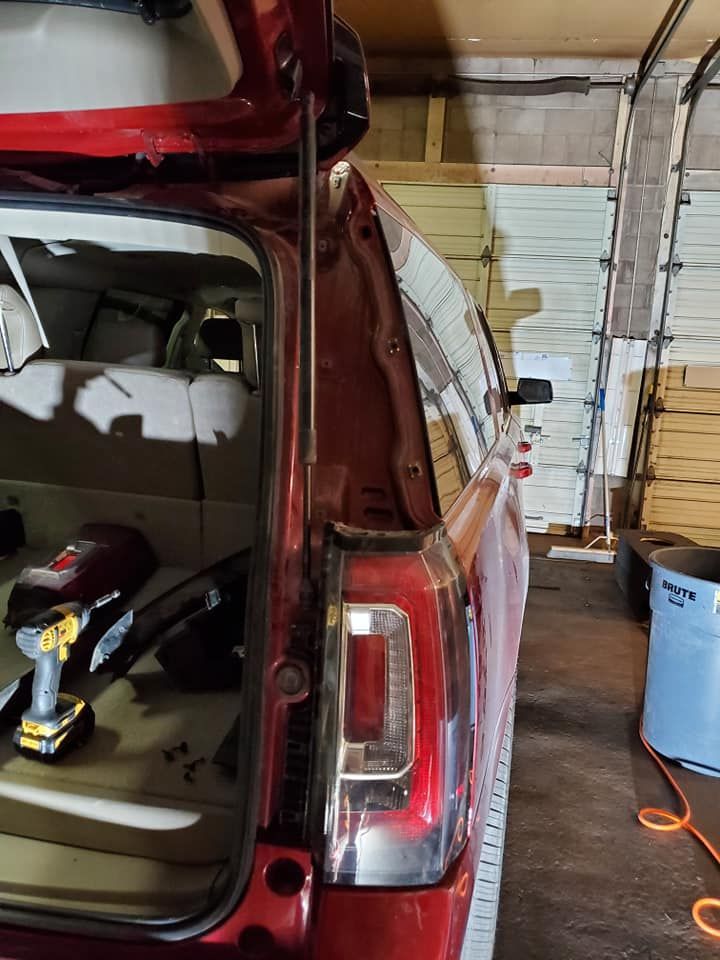 Red SUV's open trunk reveals a taillight. Interior lights, a screwdriver, and garage details are also visible.