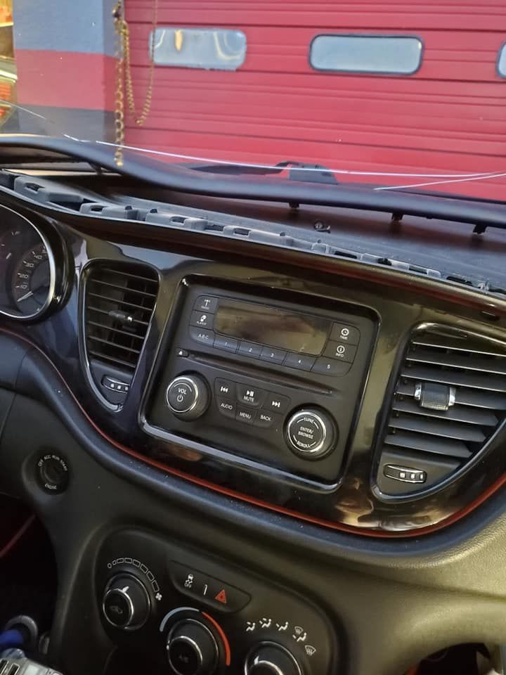 Dashboard of a car with a black stereo, air vents, and dials against a red background.