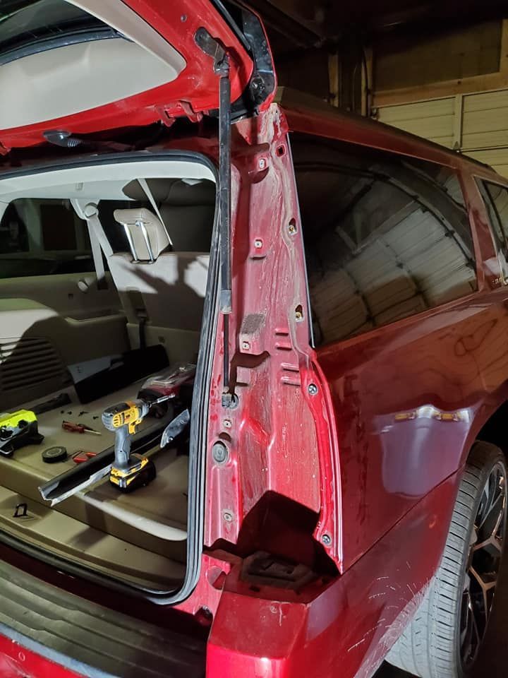 Red SUV rear door open, revealing the interior and a repair in progress. Tools lie nearby.