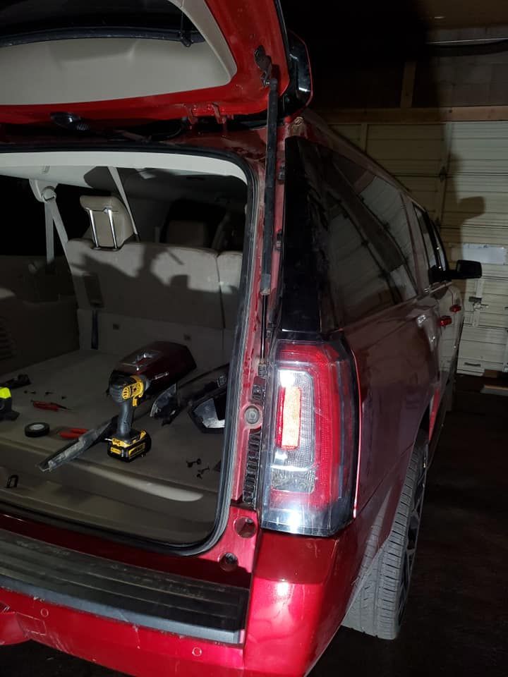 A red SUV's tailgate is open, revealing the cargo area. Tools and a taillight are visible inside. The setting is a garage.