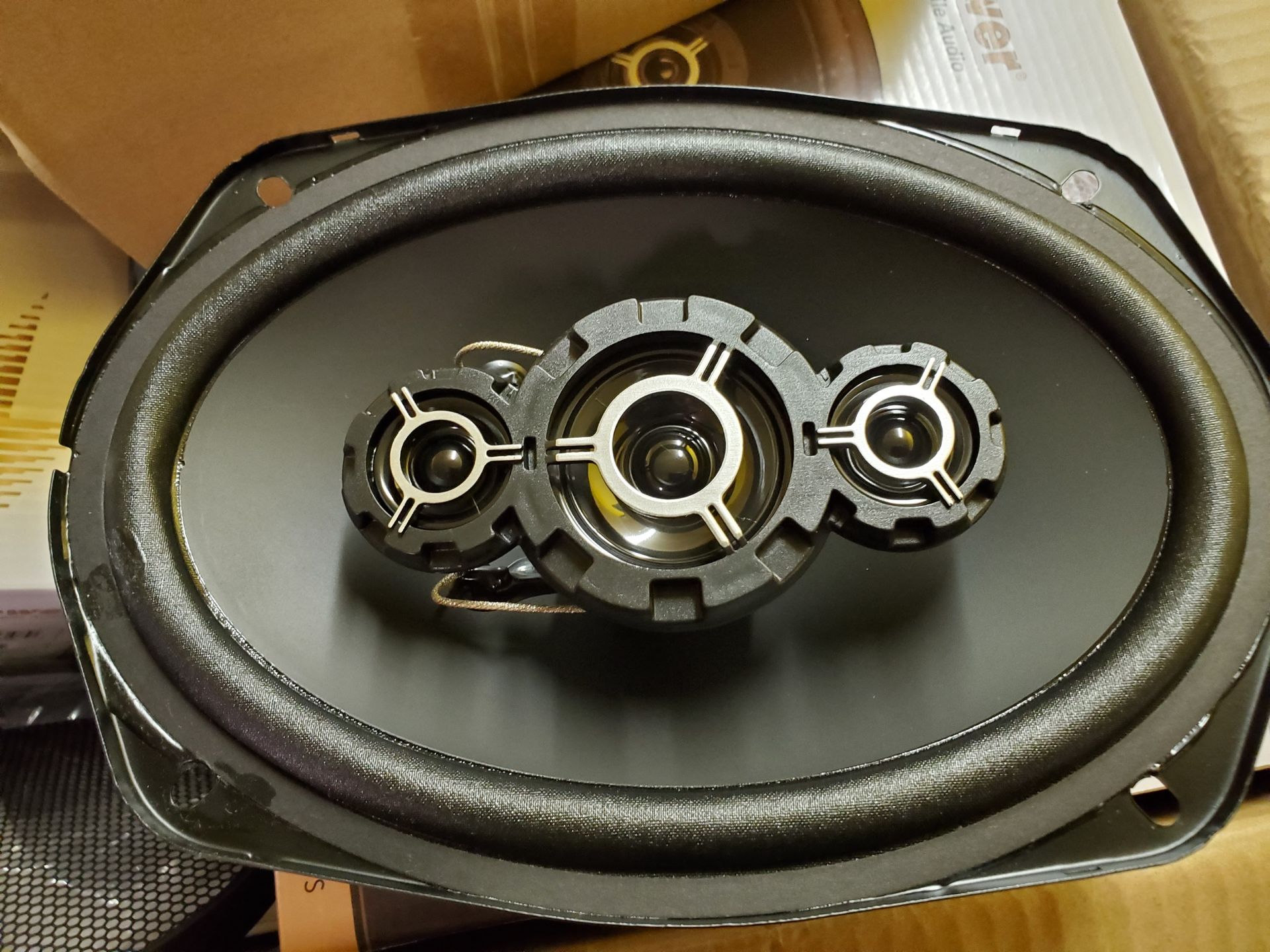 Oval car speaker with a black cone, foam surround, and three small tweeters mounted in the center.