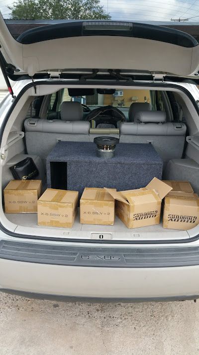Car trunk filled with cardboard boxes and a subwoofer box, likely for car audio installation. The trunk is open.