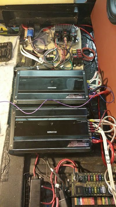 Car audio system with two amplifiers, wiring, and a fuse box installed in a vehicle. Black, red, and white wires are visible.