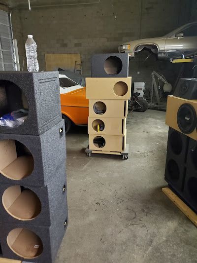 Several speaker boxes stacked in a garage, some black, some tan. 