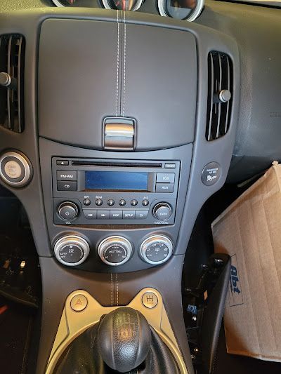 Interior dashboard of a black car, likely a Nissan 370Z, showing the radio, air vents, and gear shift.