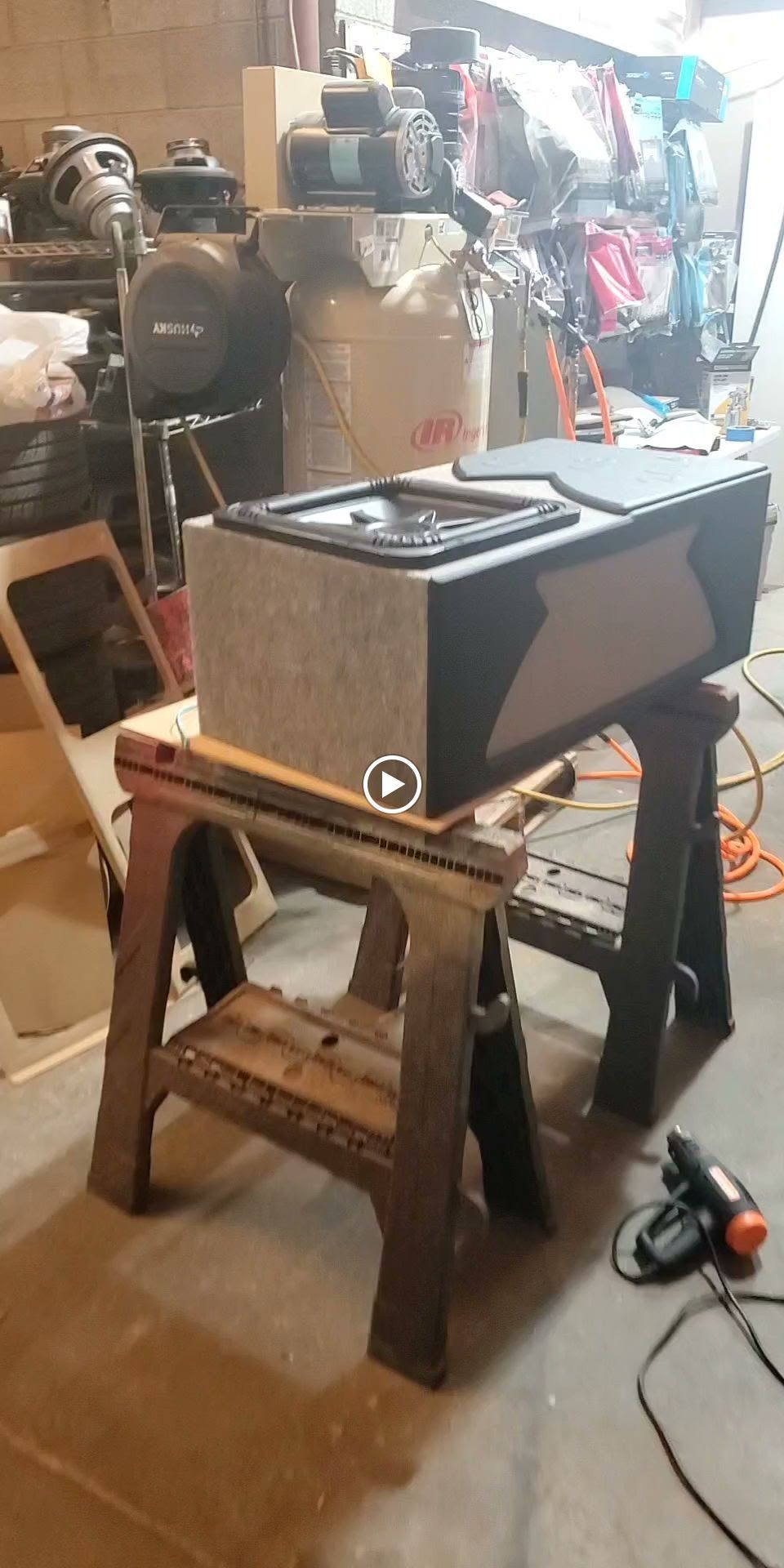 A black and gray box on a wooden sawhorse in a cluttered workshop.