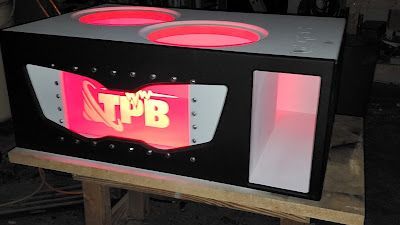 Black car audio subwoofer box with red interior lighting. Features two circular speaker openings and a side port with a logo.