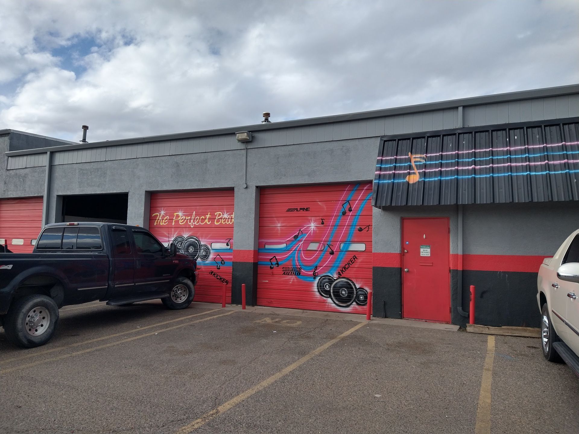 A commercial building with red garage doors featuring graffiti art, a black truck, and overcast sky.
