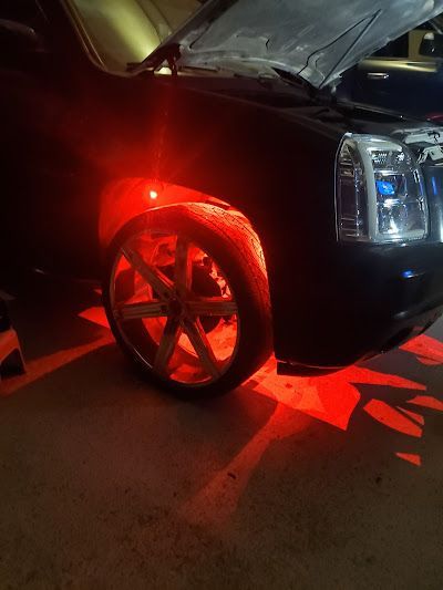 Black car with red underglow lighting up the wheel and ground; the hood is open.
