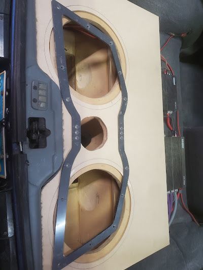 A wooden subwoofer box with two circular cutouts, a center port, and a decorative metal frame, likely for car audio.