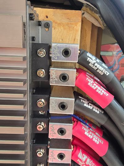 Close-up of electrical connections with black and red cables. Wires are connected to silver terminals mounted on wood.