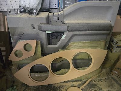 Car door panel with custom wood speaker enclosures being built in a workshop.