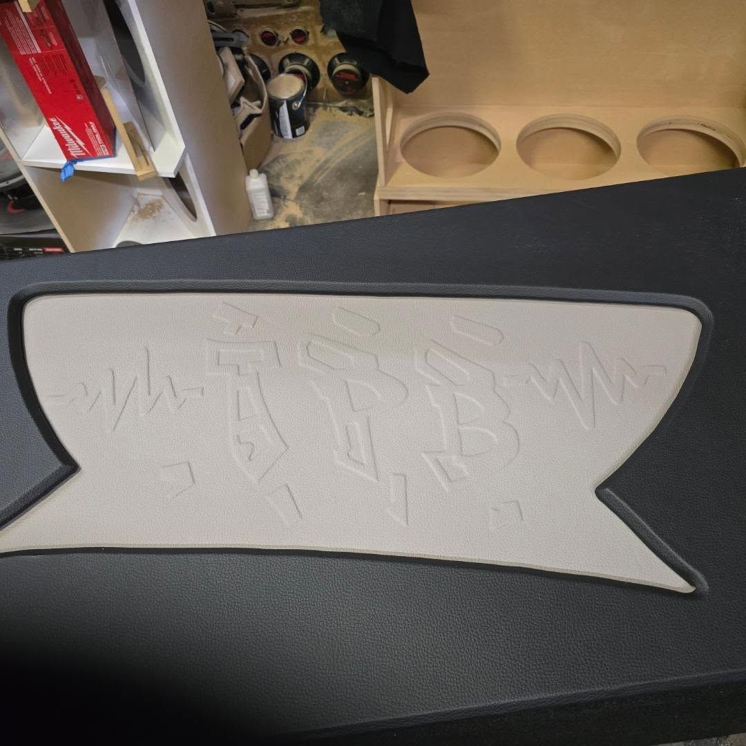 A black car audio subwoofer box with a light-colored, textured accent piece; other car audio components visible.