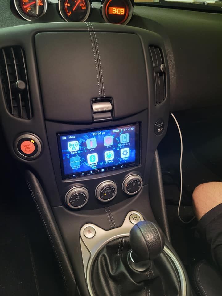 Interior view of a black car dashboard, modified with a touchscreen display and a manual gear shift. Three gauges sit above.