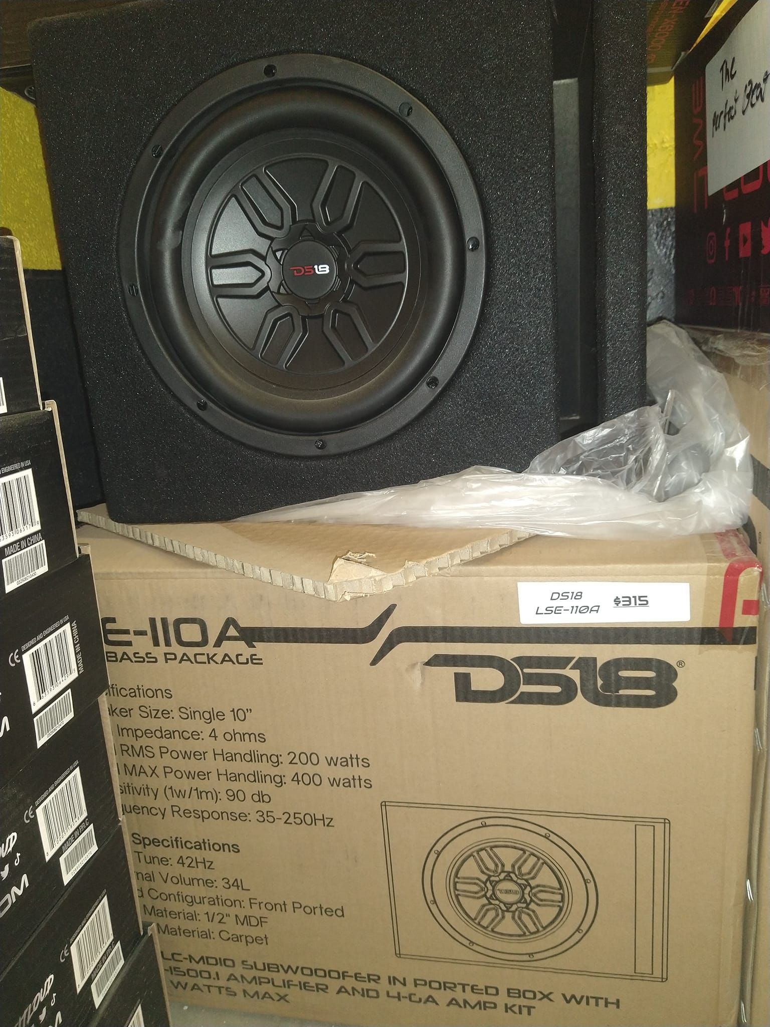 DS18 subwoofer in a black box.  The box is atop a cardboard box with product info.