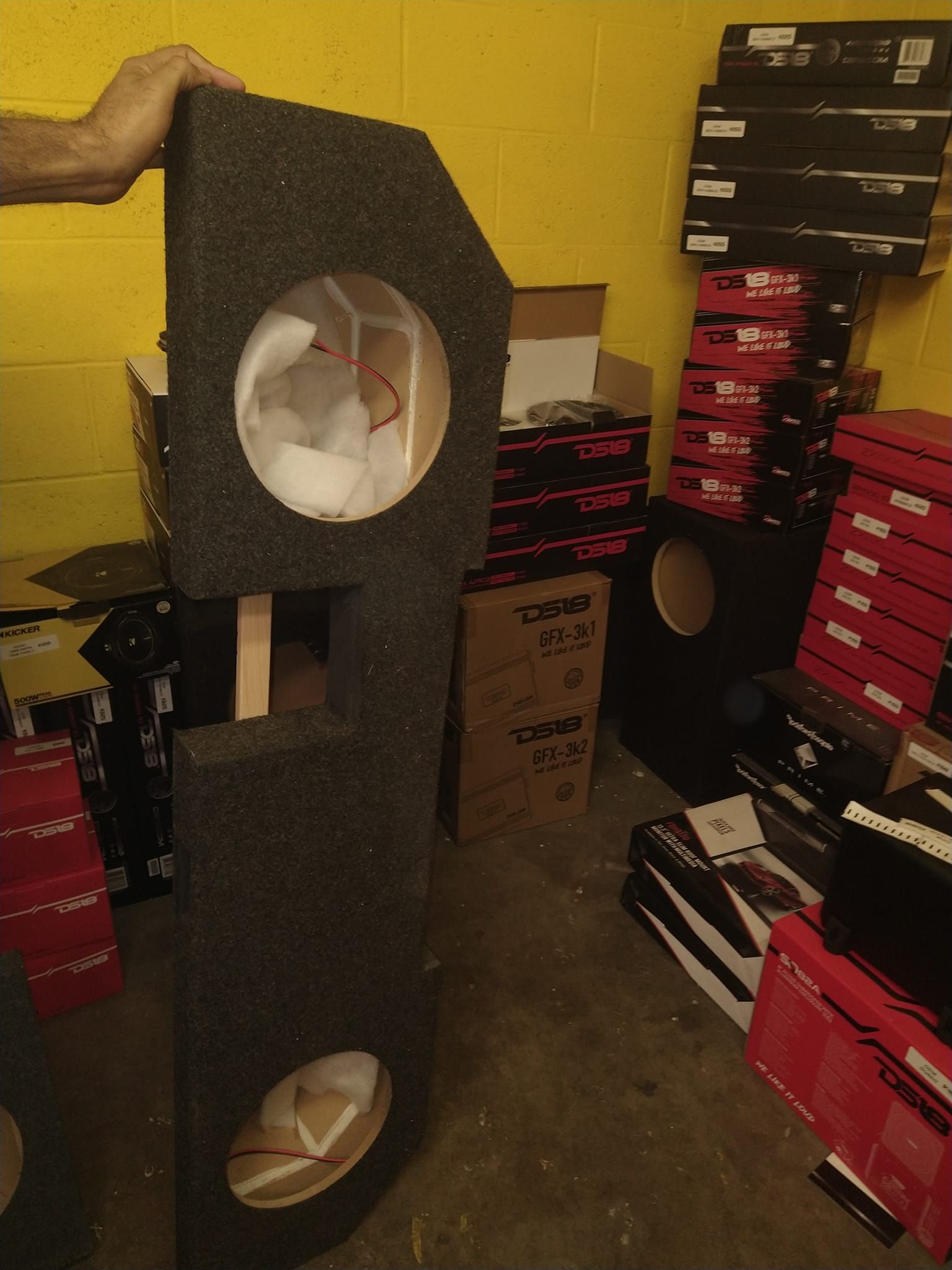 A person holds a tall, black, angled speaker box with two circular openings, likely for speakers.