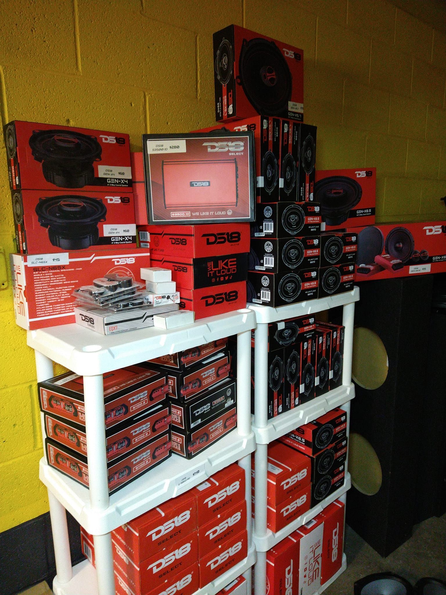 A display of car audio equipment, with various boxed speakers, amplifiers, and a head unit arranged on shelves.