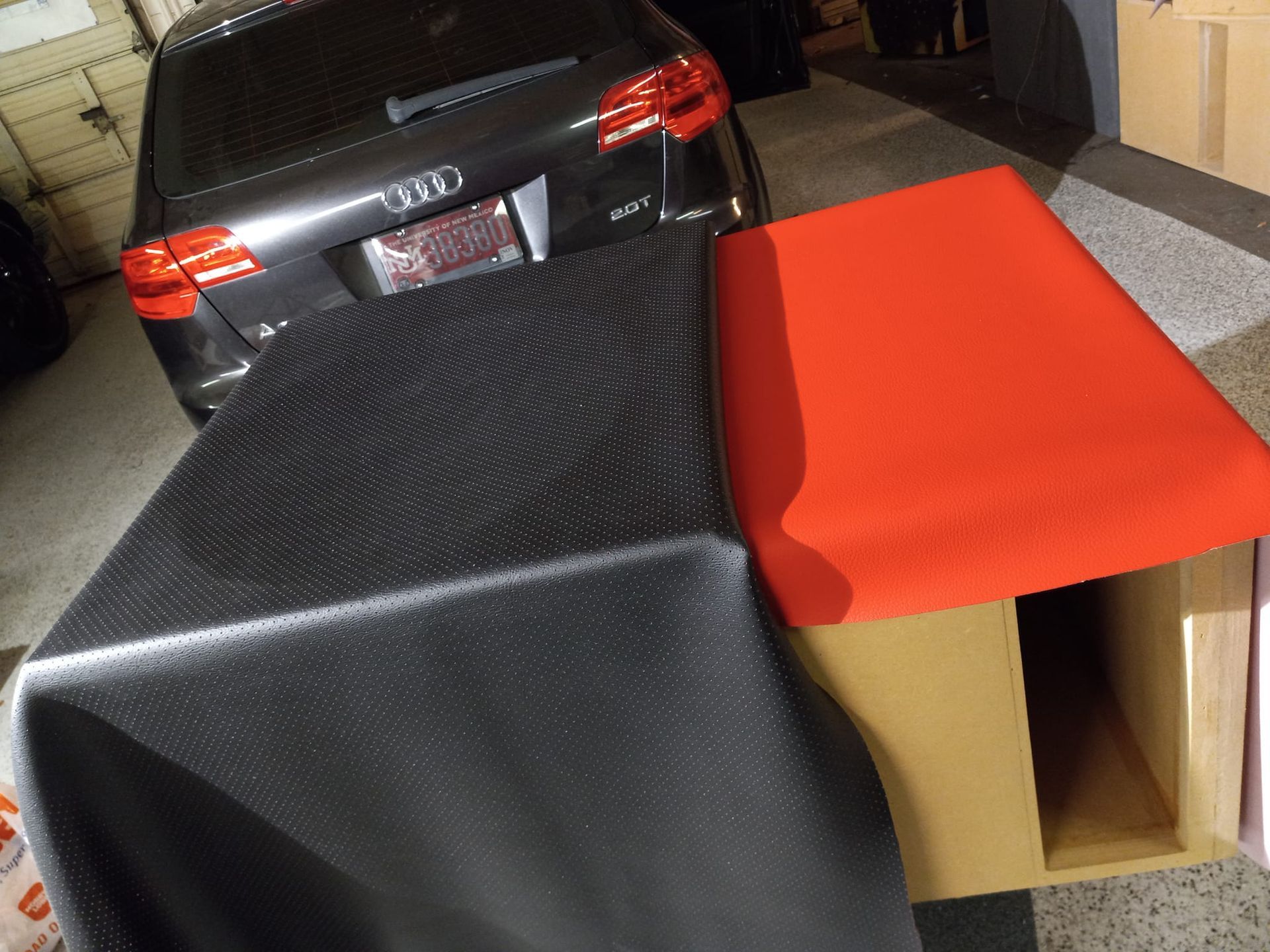 A black car with a red seat and a black cloth lying on a cardboard box, outdoors.