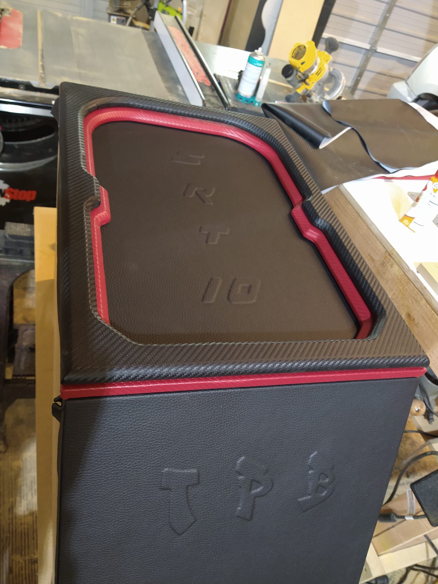A textured black box with red trim and lettering, possibly an audio enclosure, in a workshop setting.