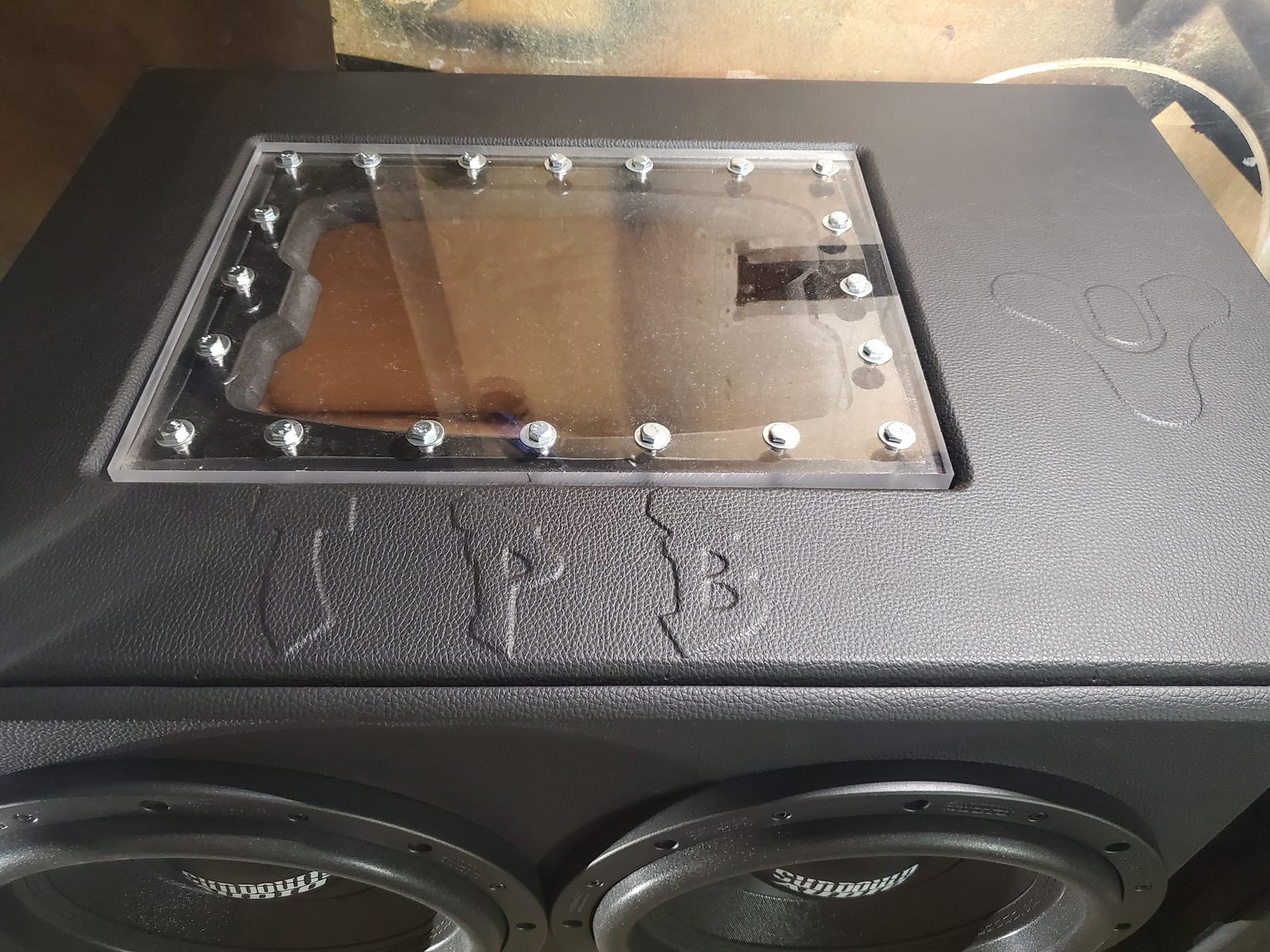 A black subwoofer enclosure with two visible speakers and a clear window secured with screws.