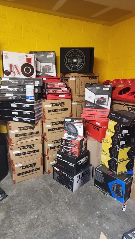 A stack of car audio equipment boxes in a storage room. Boxes are various brands and colors.