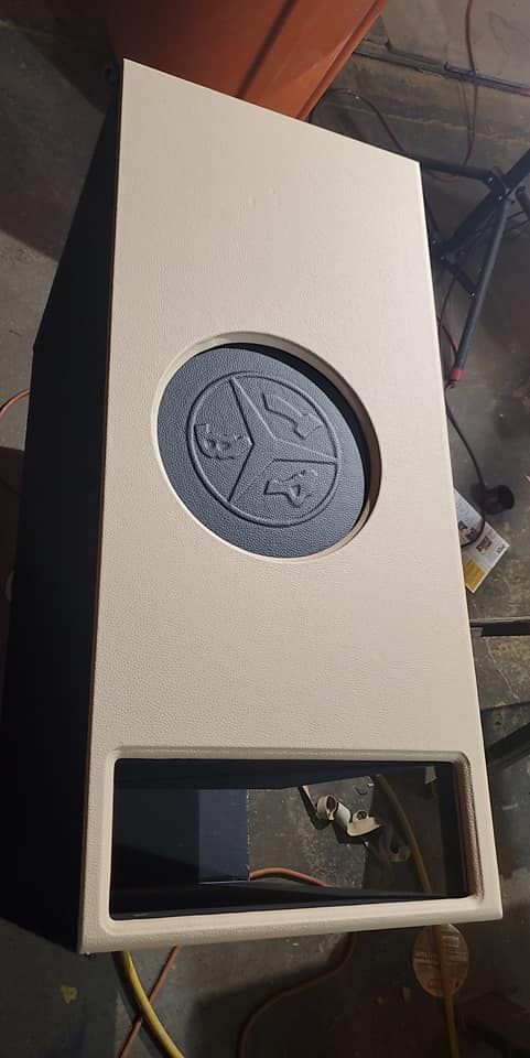 A rectangular tan speaker box with a circular speaker and rectangular opening below.