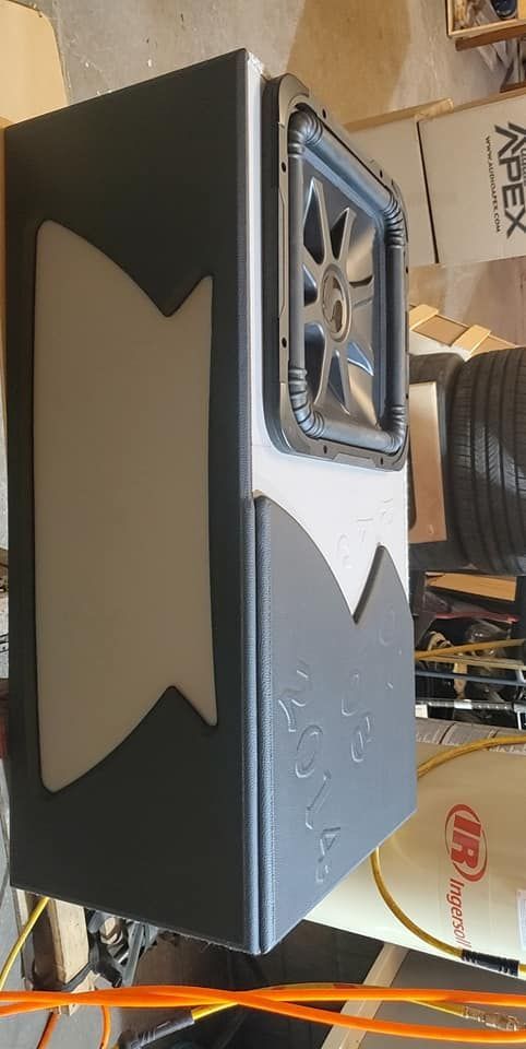 A custom subwoofer enclosure with a gray and white design. It features a Kicker subwoofer and is in a garage setting.