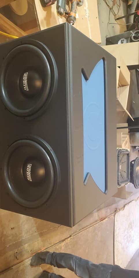 A dual subwoofer enclosure, painted dark grey, with a light blue port opening on the side.