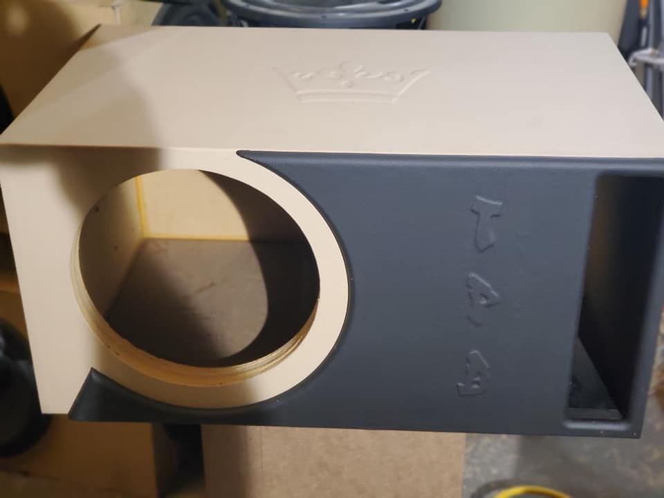 A custom subwoofer box with a gray front panel and a beige top and sides. The front has a round cutout and embossed text.