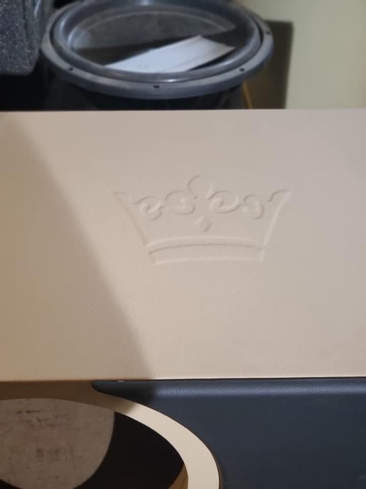 A close-up of a cream-colored amplifier with an embossed crown logo. Below, the amplifier has a black and white section.