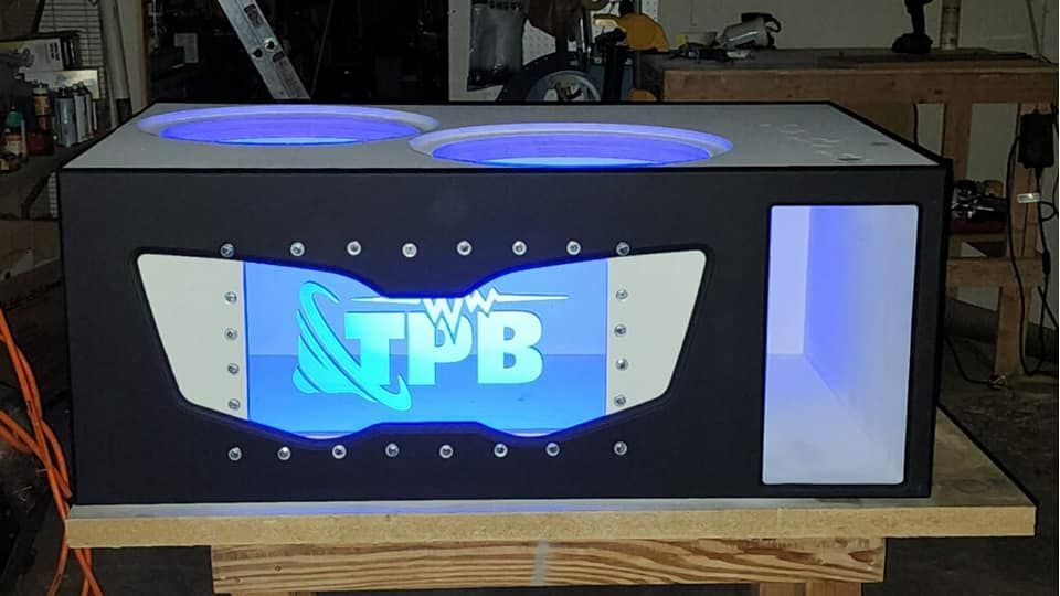 Custom car audio subwoofer box with blue LED lighting. Features the logo 