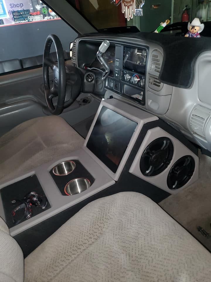 Interior of a modified truck featuring a custom center console with a large screen and two speakers, and cup holders.
