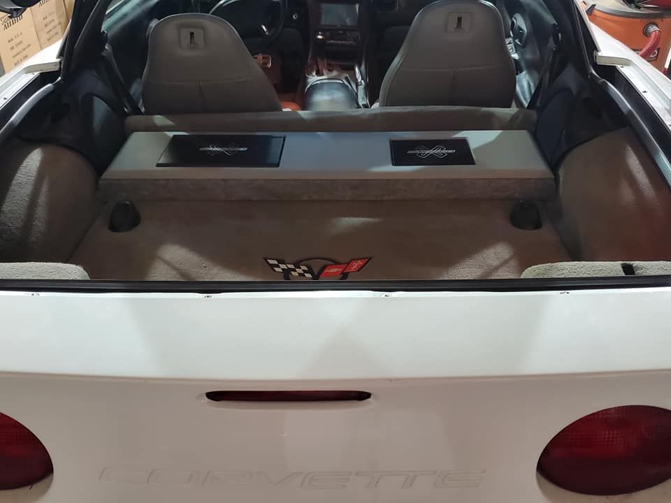 White car trunk with a customized audio system featuring amplifiers and Corvette logo.