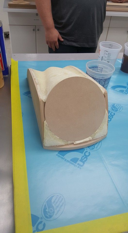 A person working on a wooden form coated with a light-colored substance, with a large circular piece attached.