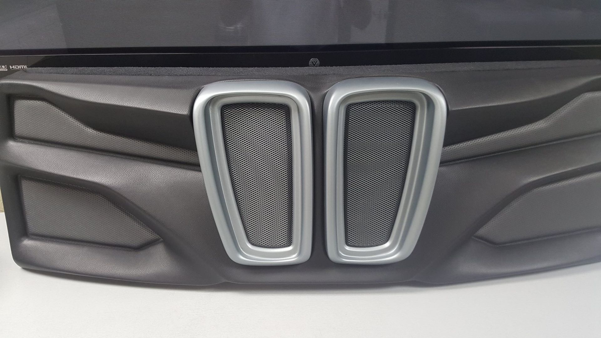 Black car dashboard panel with two silver-trimmed, mesh-filled air vents. The panel has textured, geometric designs.