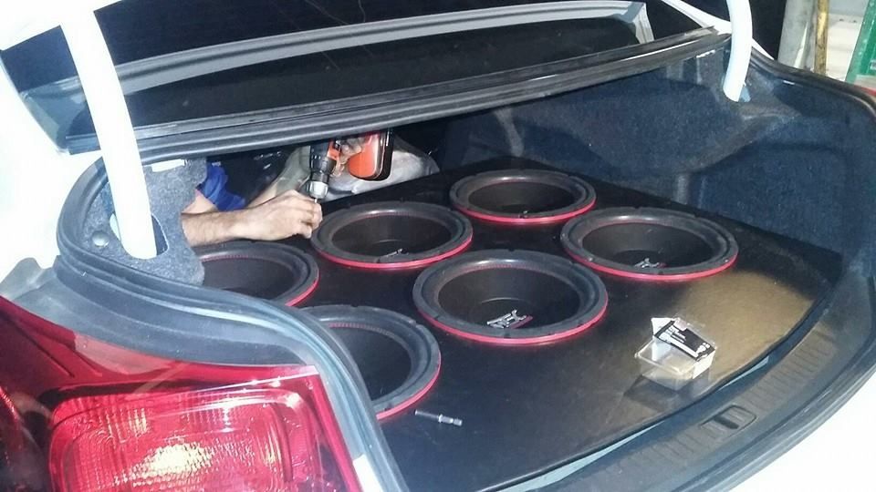 Car trunk with a custom subwoofer setup featuring six speakers and a person working on the installation.