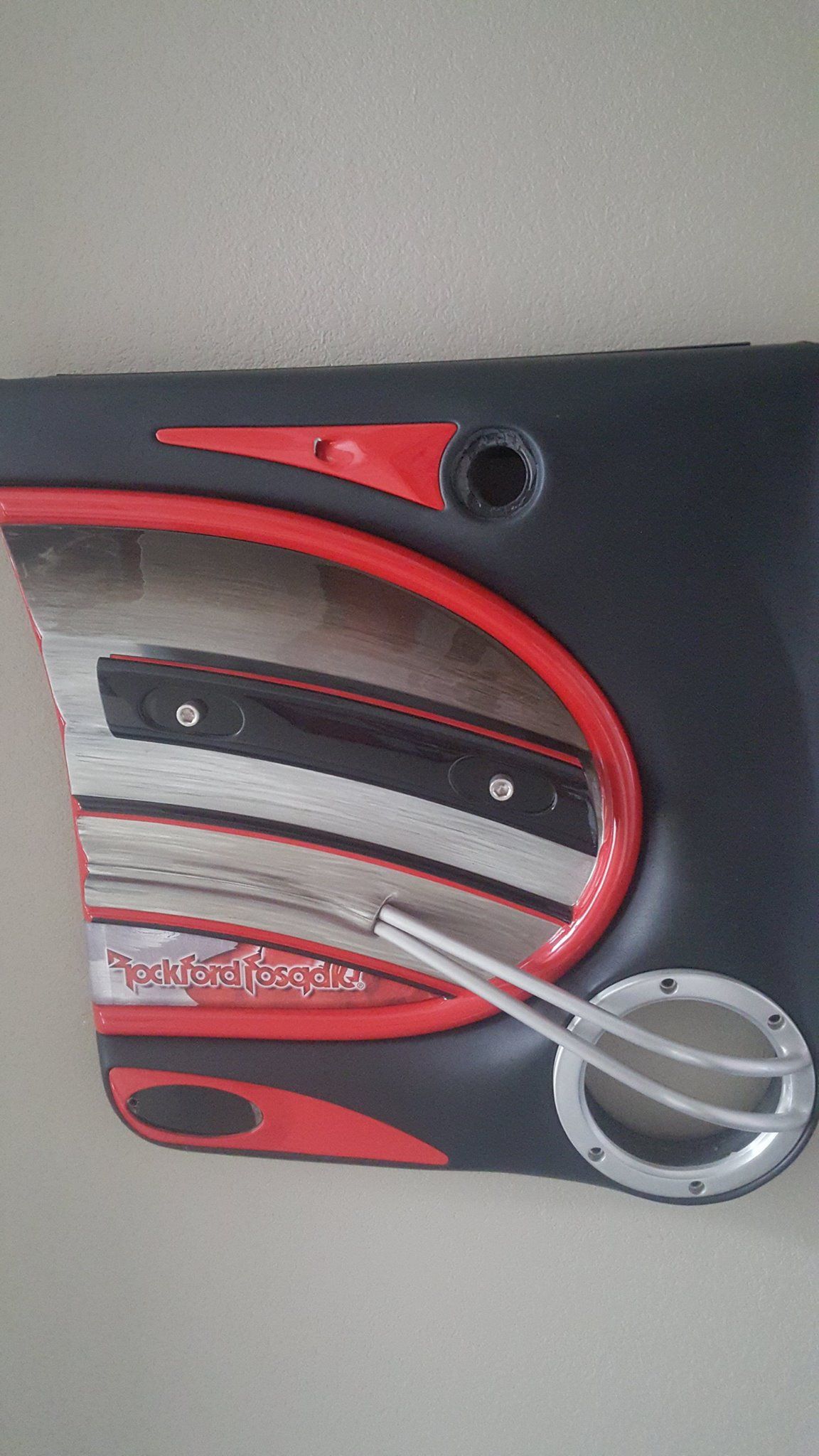 Black car door panel with red and silver accents, a circular handle, and a logo.
