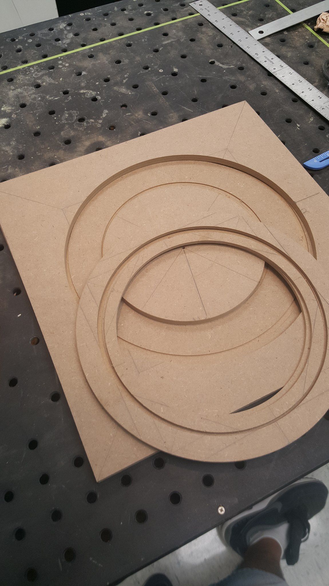 A square piece of brown fiberboard with circular and semi-circular cutouts, likely for a woodworking project.