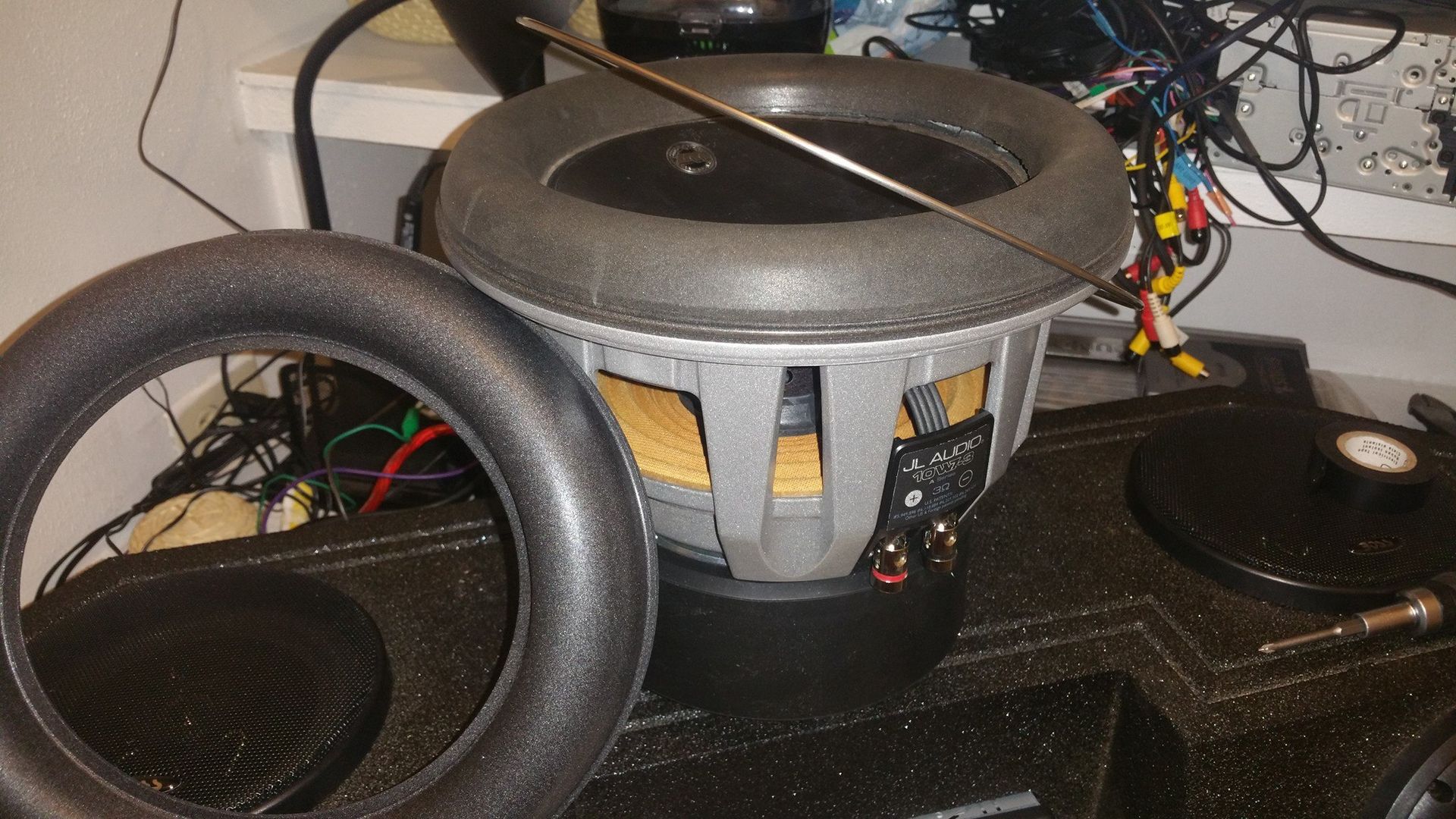 A subwoofer with its foam surround detached, sitting on a black enclosure.